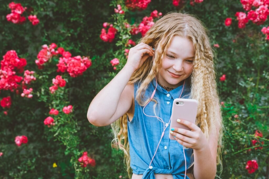 Smiling Teen girl listening to pop music on phone putting pink earphones in ears in Spotify